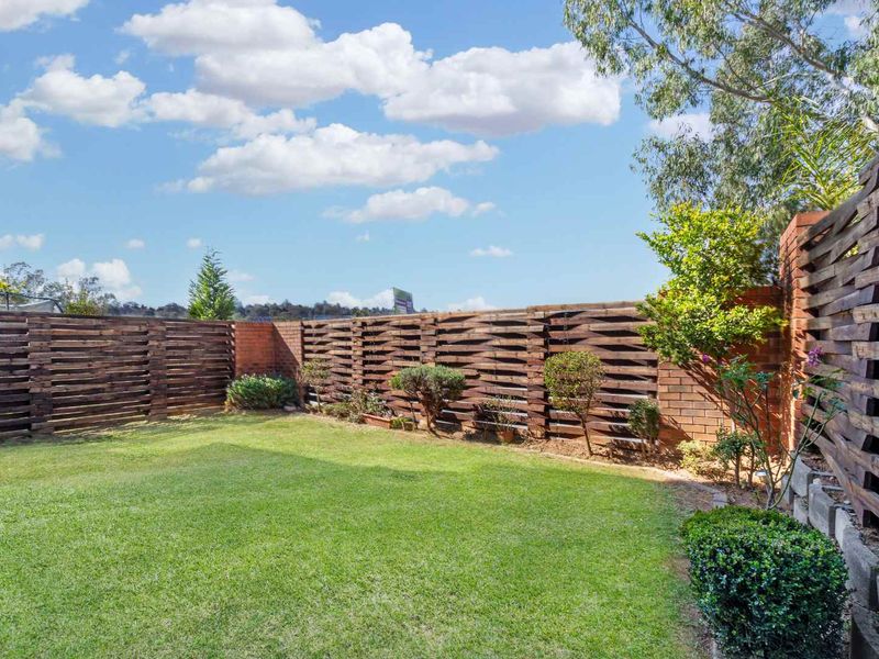 A private rear garden featuring a well-maintained lawn, enclosed by timber slat fencing and brick retaining walls.