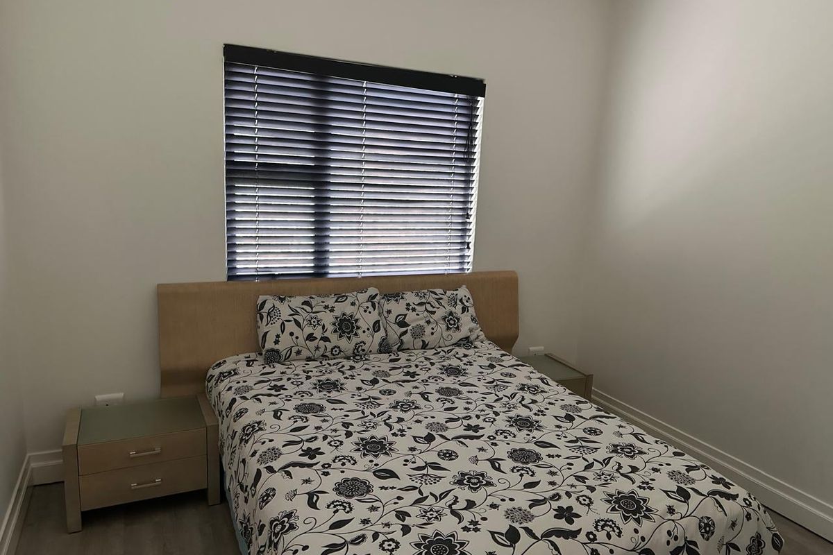 A clean and neutral bedroom featuring modern grey flooring, white walls, and fitted venetian blinds.