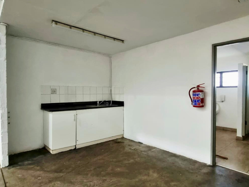 Utility space featuring a kitchenette with sink, tiled splashback, and direct access to a restroom facility within an industrial setting.