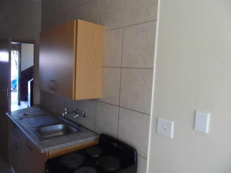 A compact kitchen area featuring built-in cabinetry, a stainless steel sink with wall-mounted faucet, tiled backsplash, and an electric stove.