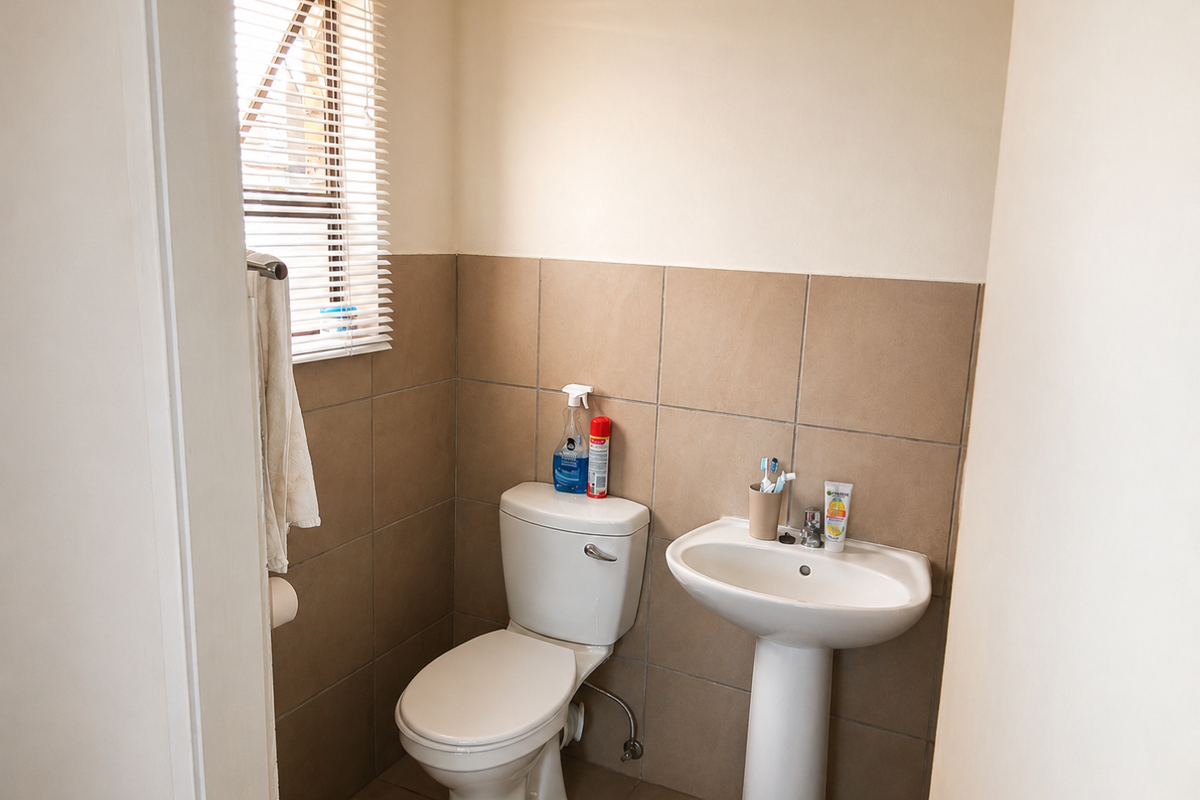 A functional guest bathroom featuring a pedestal basin, ceramic toilet, and neutral wall tiling.