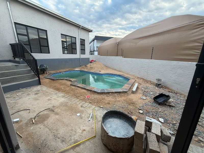 Outdoor pool area currently under construction, featuring a swimming pool, concrete patio, and boundary wall with electric fencing, awaiting final landscaping and finishing.