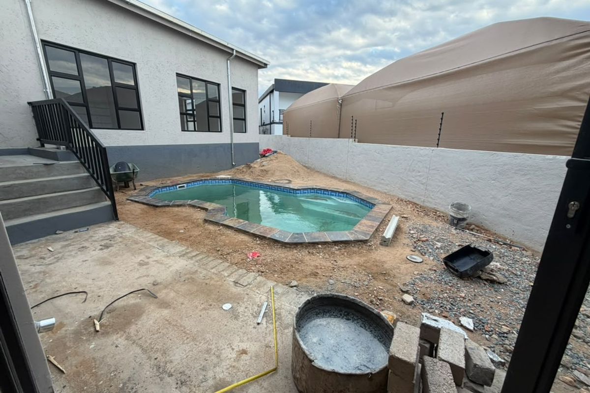 Outdoor pool area currently under construction, featuring a swimming pool, concrete patio, and boundary wall with electric fencing, awaiting final landscaping and finishing.