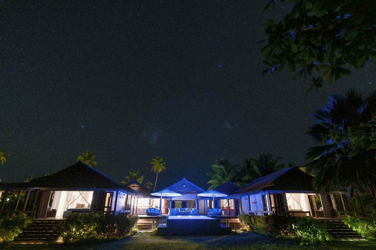 Night view of a luxury villa featuring a central swimming pool, illuminated outdoor decking, and multiple interconnected living structures under a starry sky.