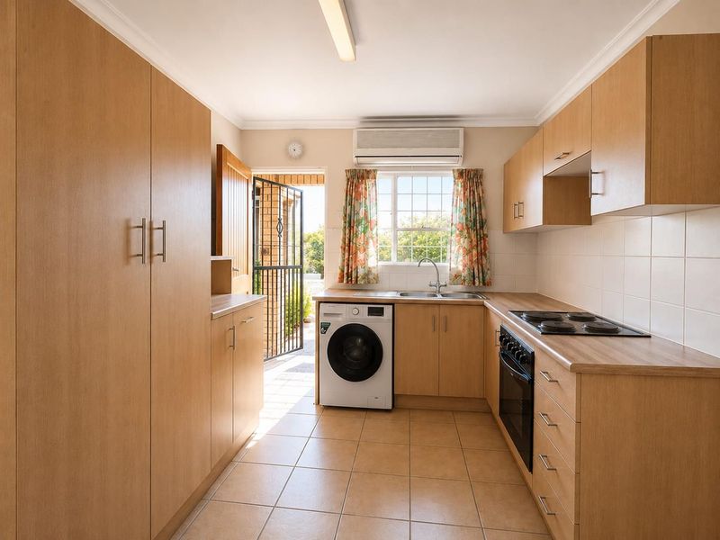 Functional kitchen featuring light wood cabinetry, laminate countertops, integrated electric hob and oven, tiled flooring, and direct access to the exterior.