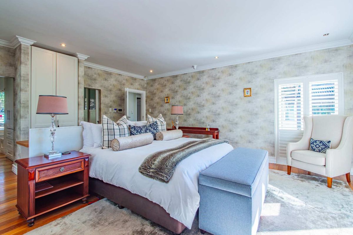 Spacious bedroom featuring timber flooring, built-in cabinetry, crown molding, and plantation shutters, offering a well-maintained and comfortable living space.