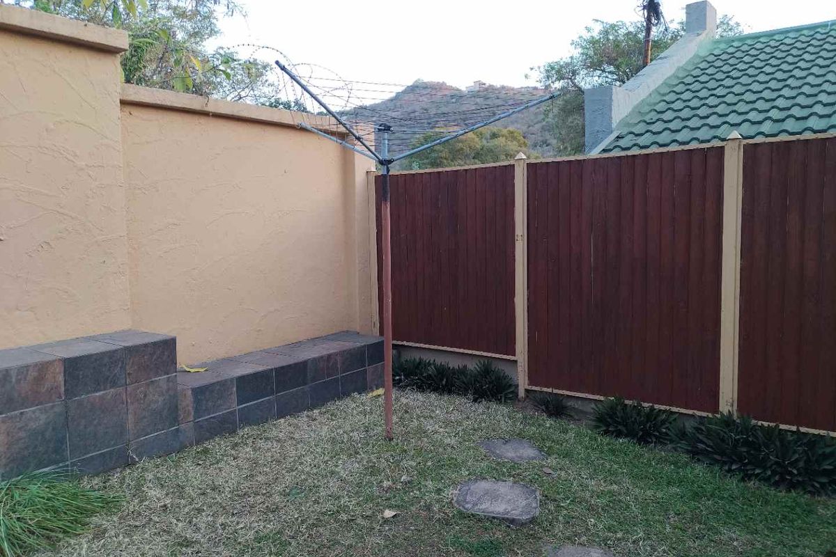 A private rear garden area featuring a tiled retaining wall, perimeter fencing, and a rotary clothesline set within a small grassed yard.