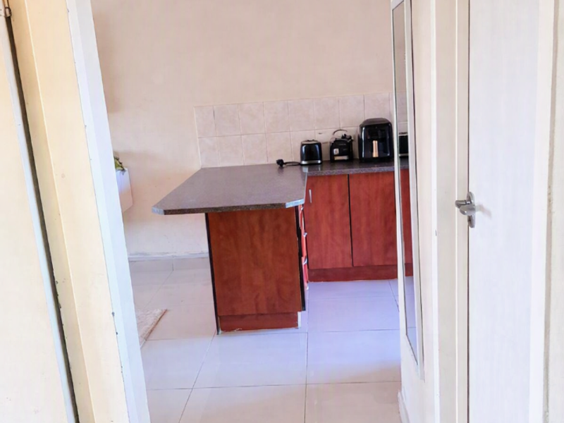 A view through a doorway into a kitchen featuring wooden cabinetry, a laminate countertop, and tiled flooring.