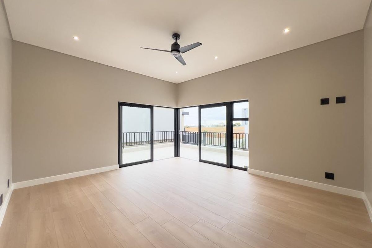 Spacious bedroom featuring light wood-look flooring, recessed ceiling lighting, a modern ceiling fan, and large sliding glass doors opening to a private balcony.