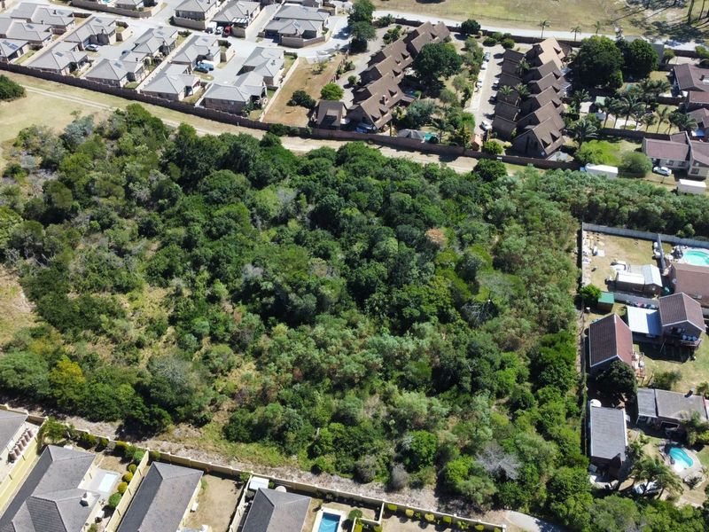 An aerial view of a vacant residential plot surrounded by established suburban housing and dense vegetation.