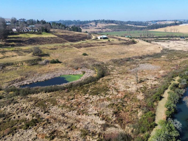 An aerial view of the vacant residential land featuring natural landscape, a small pond, and a river running through the property.