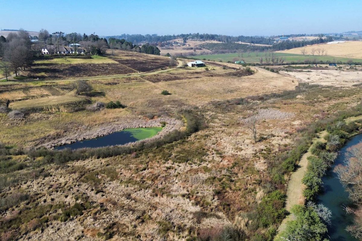 An aerial view of the vacant residential land featuring natural landscape, a small pond, and a river running through the property.