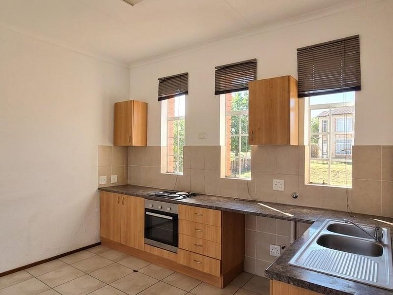 A functional kitchen featuring light wood cabinetry, laminate countertops, a built-in oven and hob, and a stainless steel sink with tiled backsplash.