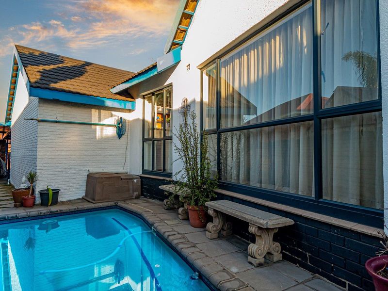 A well-maintained outdoor pool area featuring a tiled surround, large windows, and a clean painted brick exterior facade.