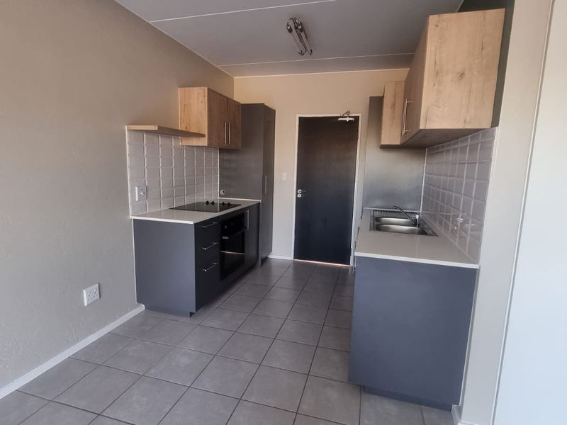 Modern galley-style kitchen featuring dark grey base cabinets, light wood upper cupboards, stone countertops, built-in oven and hob, and tiled flooring.