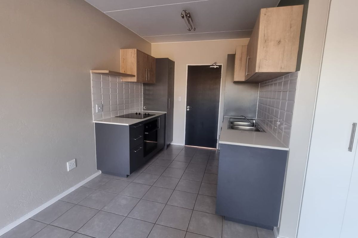 Modern galley-style kitchen featuring dark grey base cabinets, light wood upper cupboards, stone countertops, built-in oven and hob, and tiled flooring.