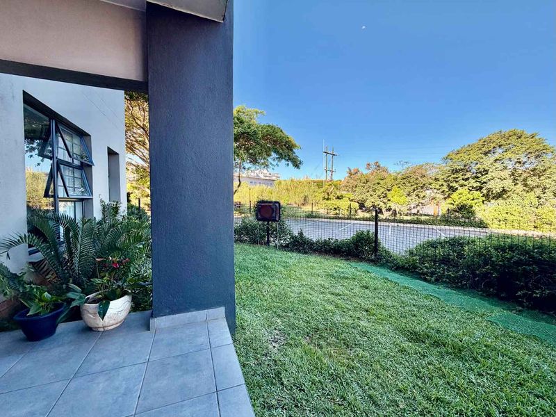 A covered patio area featuring tiled flooring and a concrete pillar, overlooking a private garden space with perimeter fencing.