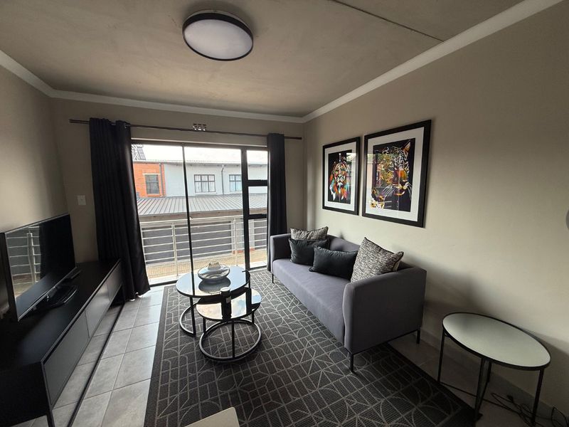 A well-maintained living room featuring tiled flooring, a ceiling light fixture, and a sliding glass door that opens onto a balcony.