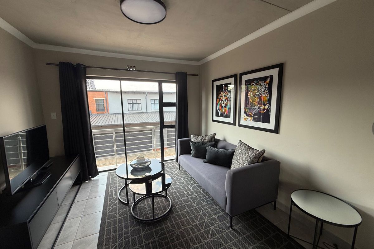 A well-maintained living room featuring tiled flooring, a ceiling light fixture, and a sliding glass door that opens onto a balcony.