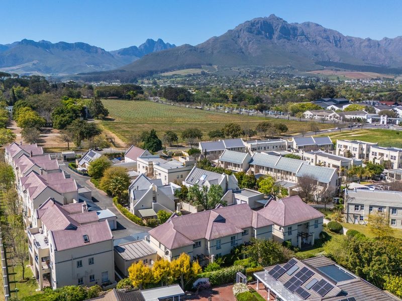 An aerial view of a residential apartment complex featuring pitched roofs, solar panels, and landscaped grounds set against a mountain backdrop.
