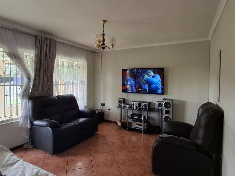 A comfortable living room featuring tiled flooring, a ceiling light fixture, and access to an outdoor area through a sliding door with security gate.