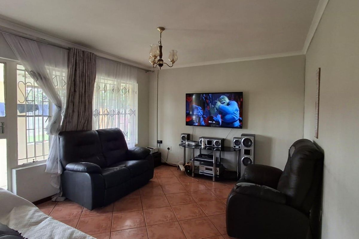 A comfortable living room featuring tiled flooring, a ceiling light fixture, and access to an outdoor area through a sliding door with security gate.