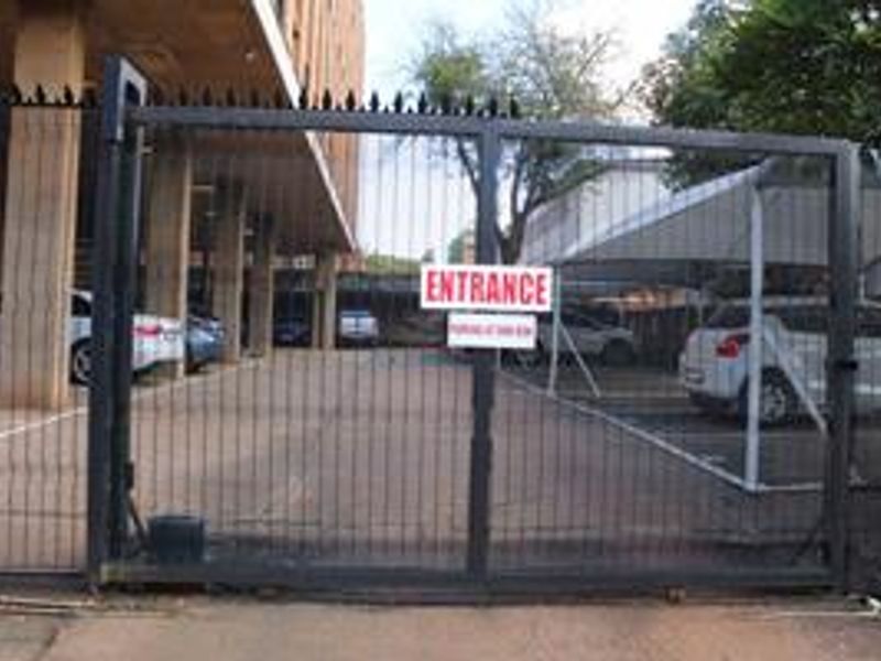 A secure gated entrance leading to a covered parking area with concrete structural supports.