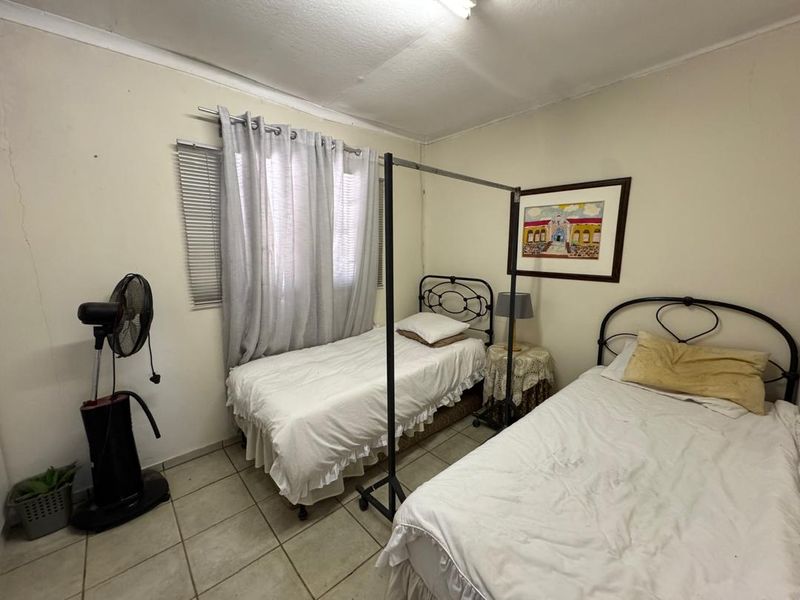 A functional bedroom featuring tiled flooring and venetian blinds, showing signs of wear including visible wall cracks.