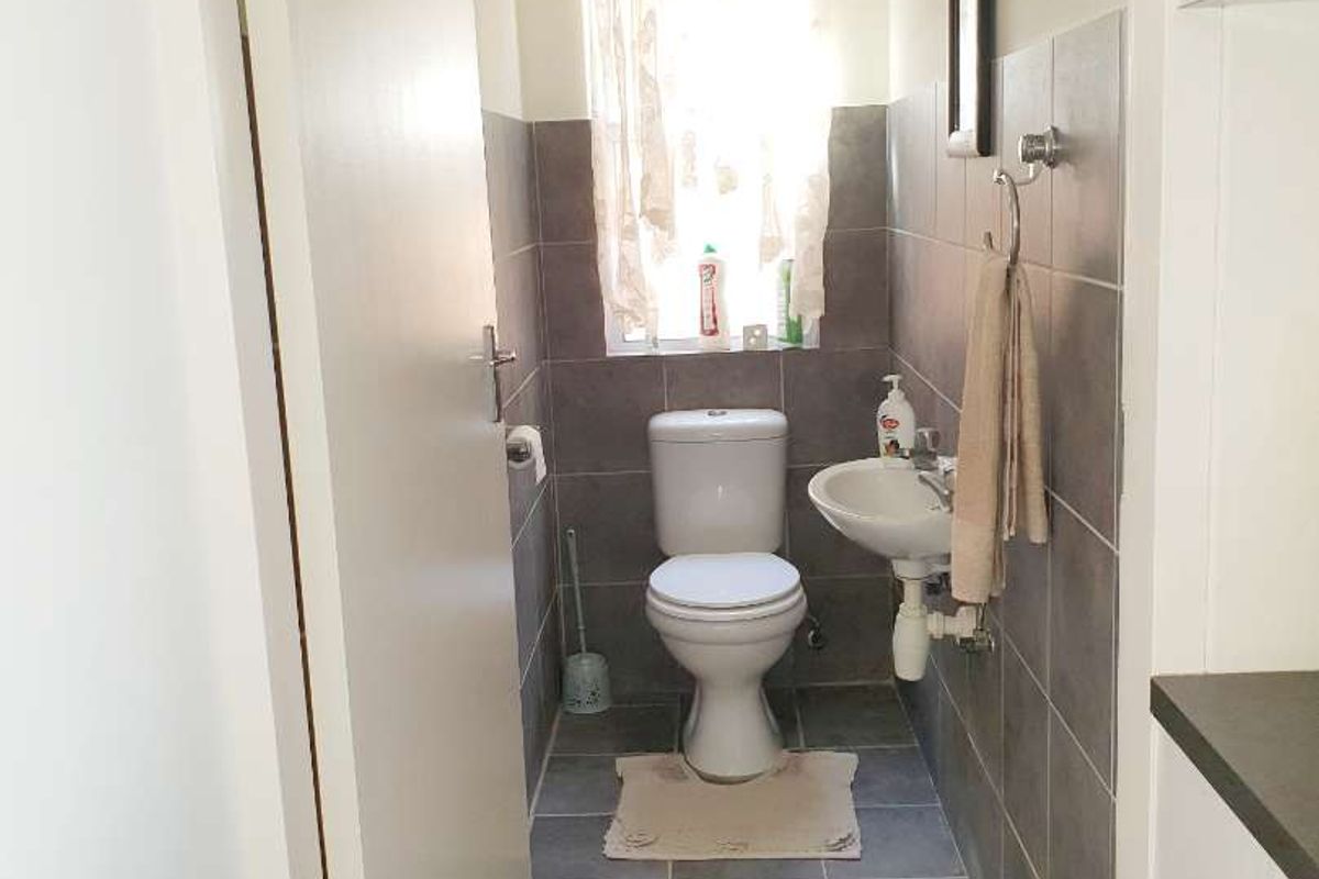 A compact guest bathroom featuring grey floor and wall tiling, a white toilet, and a small wall-mounted basin.