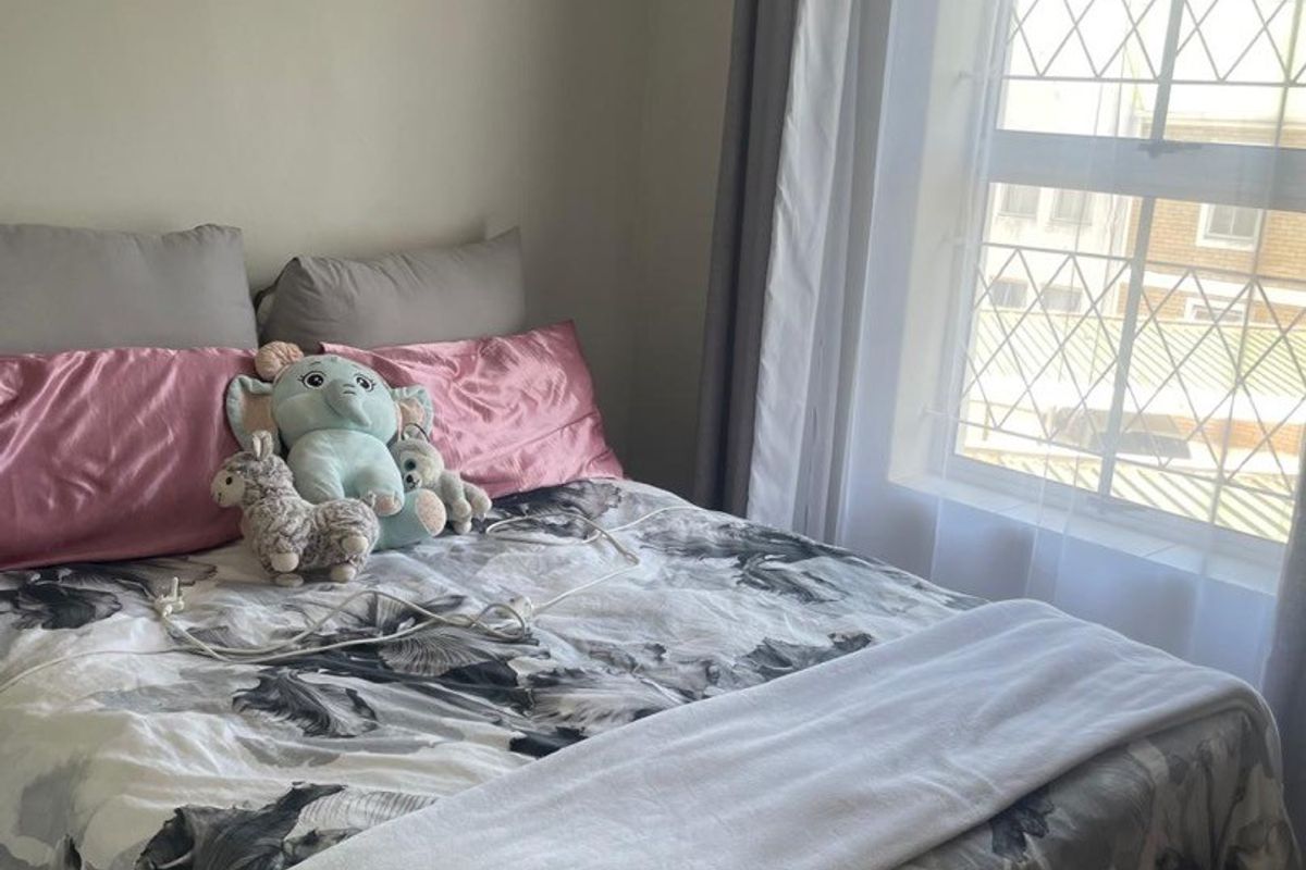 A cozy bedroom featuring tiled flooring and a window fitted with security bars, providing natural light and a view of the exterior.