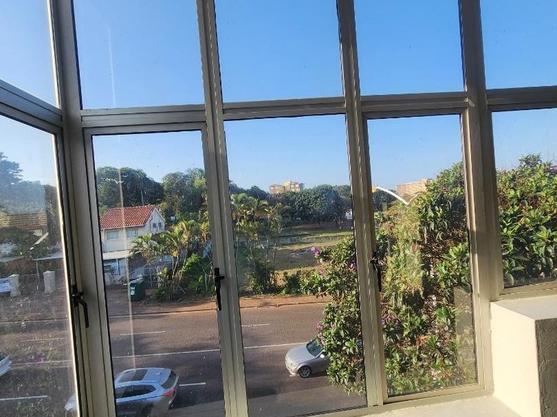 Enclosed balcony area featuring large aluminium-framed windows with views of the street and surrounding neighbourhood.