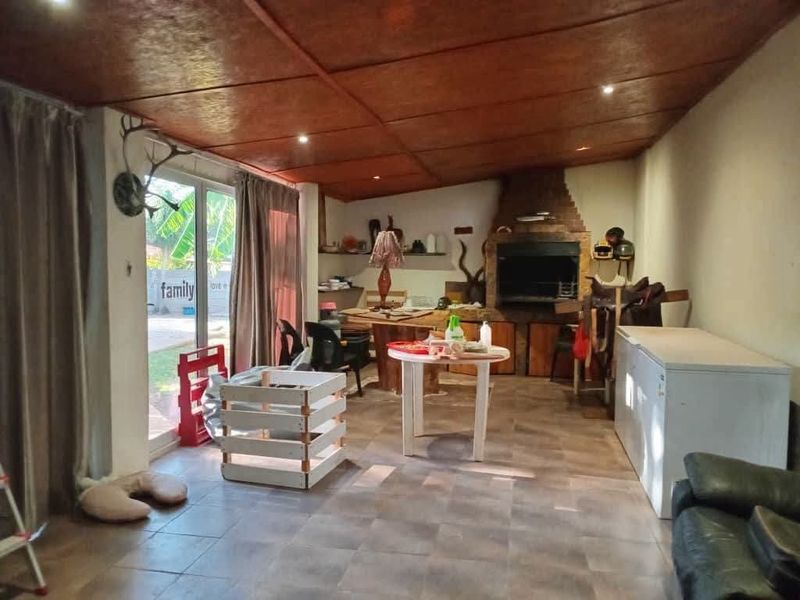Covered patio area featuring a built-in braai, tiled flooring, and sliding glass doors leading to the garden.