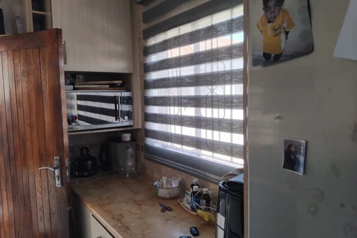 A compact kitchen area featuring built-in cabinetry, a laminate countertop, and a window with fitted roller blinds.