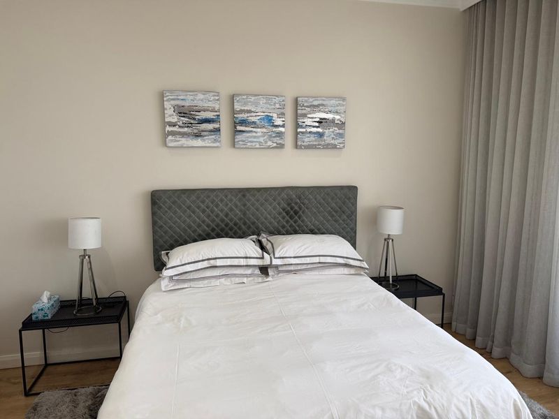 A well-maintained bedroom featuring neutral wall tones, laminate flooring, and floor-to-ceiling curtains, providing a clean and comfortable living space.