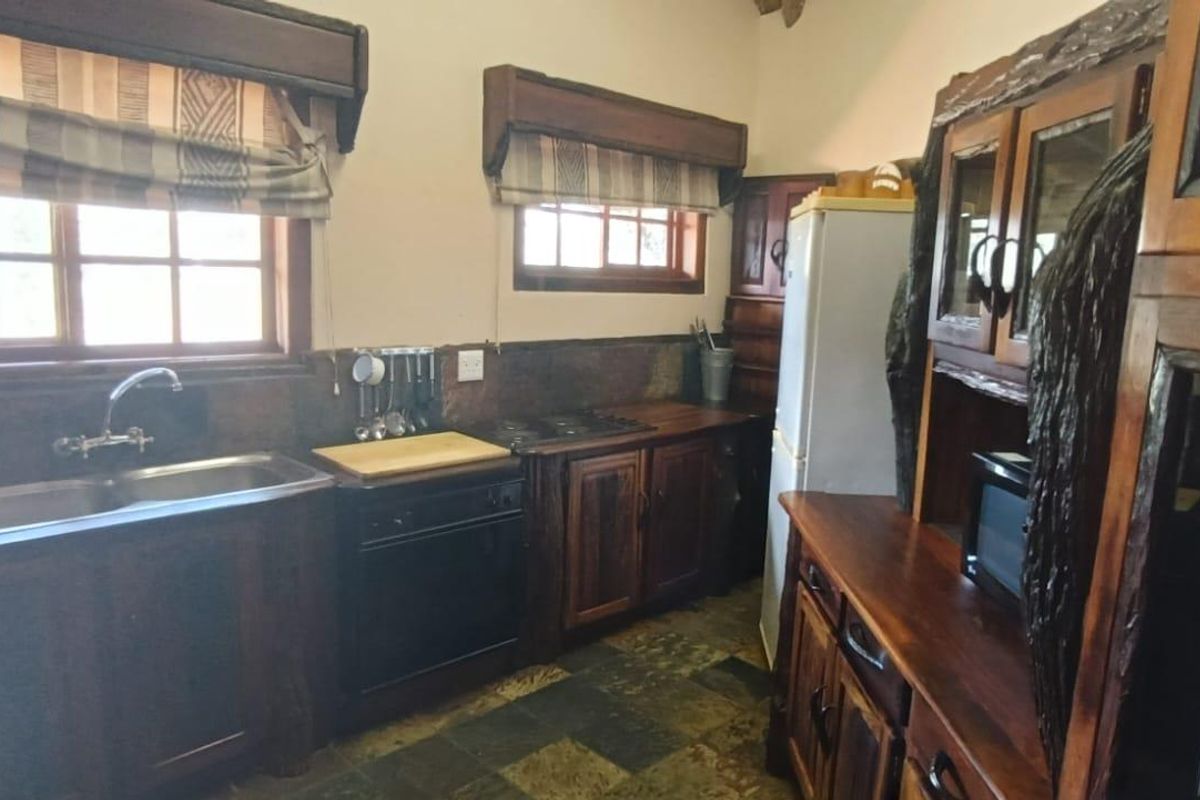 Rustic farm-style kitchen featuring custom dark wood cabinetry, integrated sink, built-in hob, and stone-style flooring with natural light.