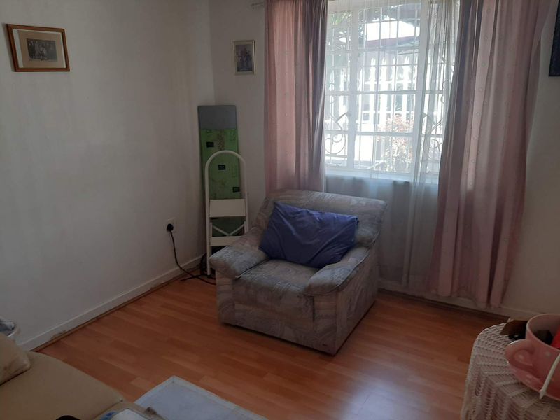 A living room featuring laminate flooring and a window fitted with security bars, offering a functional space with potential for cosmetic updates.