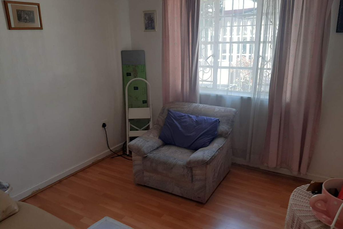 A living room featuring laminate flooring and a window fitted with security bars, offering a functional space with potential for cosmetic updates.