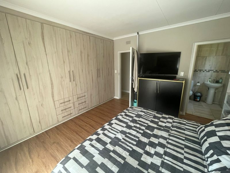Spacious bedroom featuring extensive built-in cupboards, warm laminate flooring, and direct access to an en-suite bathroom.