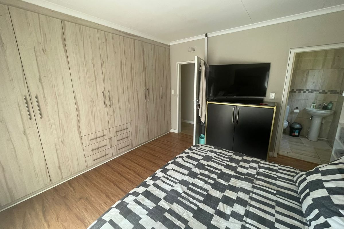Spacious bedroom featuring extensive built-in cupboards, warm laminate flooring, and direct access to an en-suite bathroom.