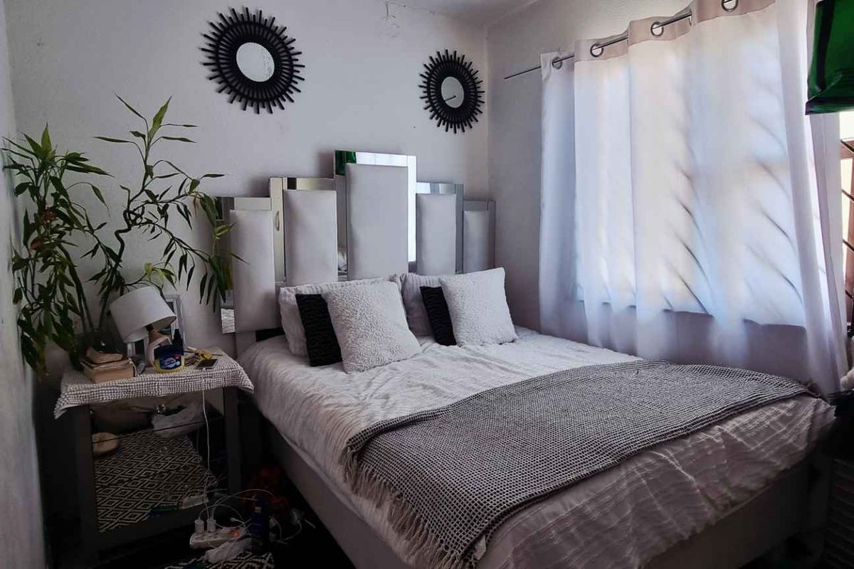 A compact bedroom featuring a window with curtains and neutral wall finishes, offering a functional space for rest.