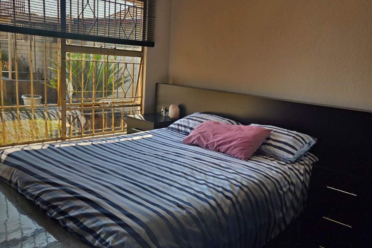 A functional bedroom featuring a built-in headboard and security bars on the window, providing a secure and practical sleeping space.