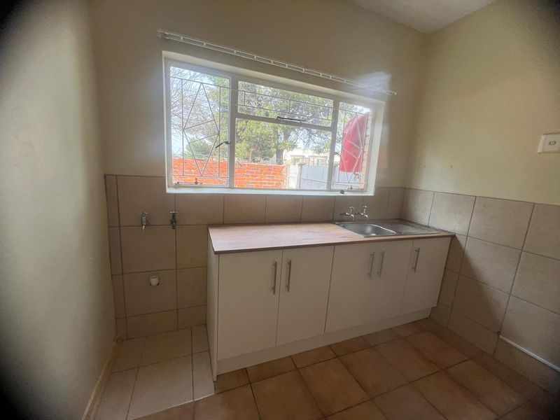 A functional kitchen area featuring built-in cabinetry, a stainless steel sink, tiled splashbacks, and tiled flooring, with security bars installed on the window.