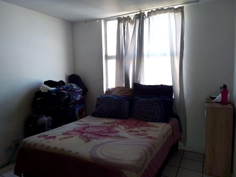 A simple bedroom featuring tiled flooring and a window with curtains, providing basic accommodation space.
