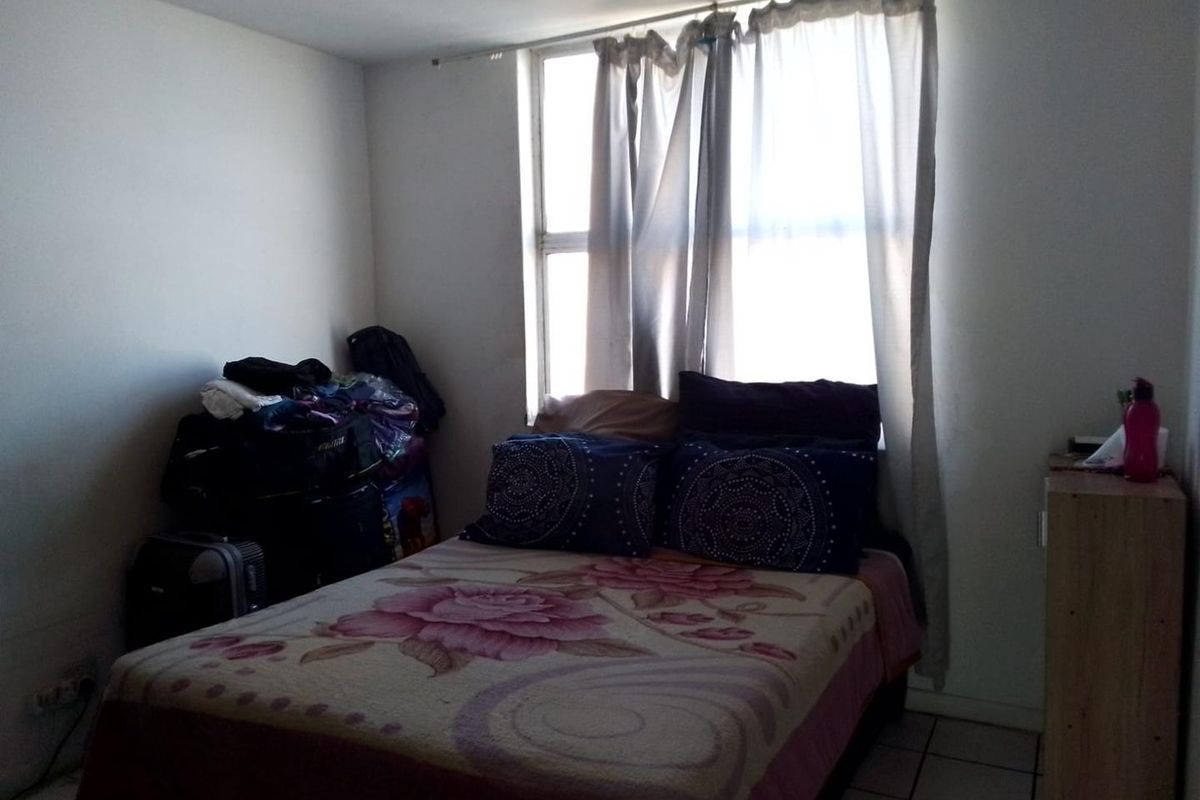 A simple bedroom featuring tiled flooring and a window with curtains, providing basic accommodation space.
