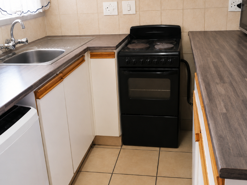A functional kitchen featuring laminate countertops, a stainless steel sink, tiled backsplash, and a freestanding electric stove with built-in cabinetry.