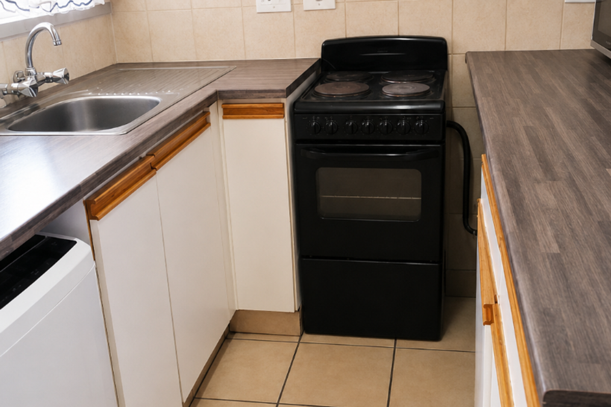 A functional kitchen featuring laminate countertops, a stainless steel sink, tiled backsplash, and a freestanding electric stove with built-in cabinetry.