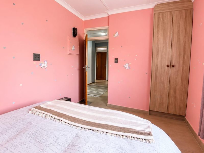 A bedroom featuring pink walls, built-in wooden wardrobe, and coving, providing a functional space with direct access to the hallway.