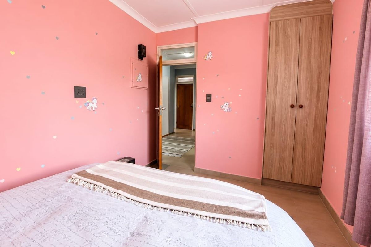 A bedroom featuring pink walls, built-in wooden wardrobe, and coving, providing a functional space with direct access to the hallway.