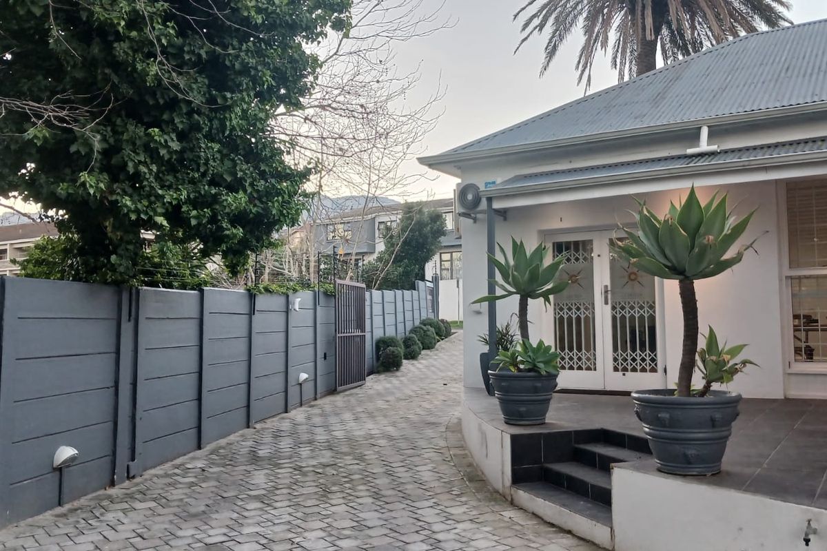 Rear exterior view featuring a paved driveway, secure boundary walling, and a tiled patio area leading to the office entrance.