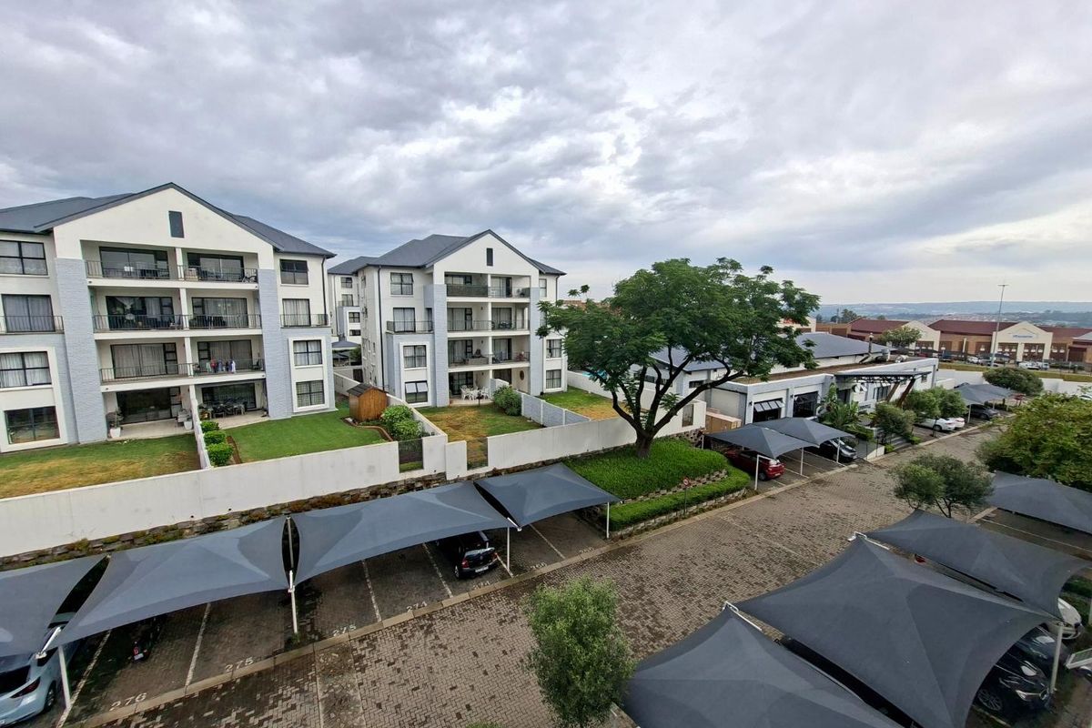 An elevated aerial view of a modern apartment complex featuring paved parking with shade cloth carports and well-maintained landscaped grounds.